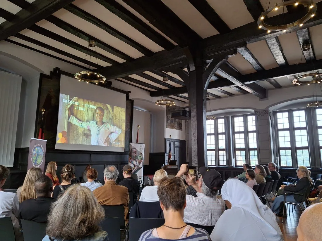 Publikum in einem historischen Saal blickt auf eine Leinwand mit der Aufschrift „SAFEGIRL – Sierra Leone“.