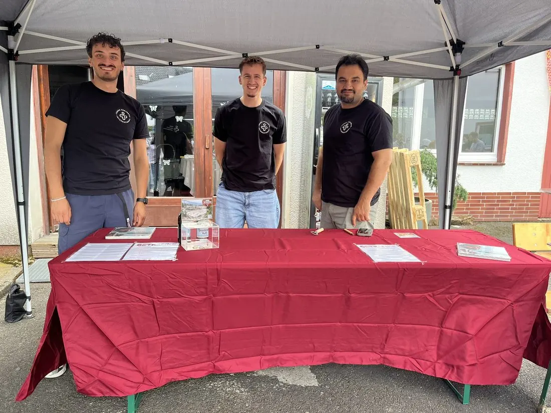 Drei junge Teammitglieder in TERRA-Shirts stehen hinter einem Tisch auf einem Fest.
