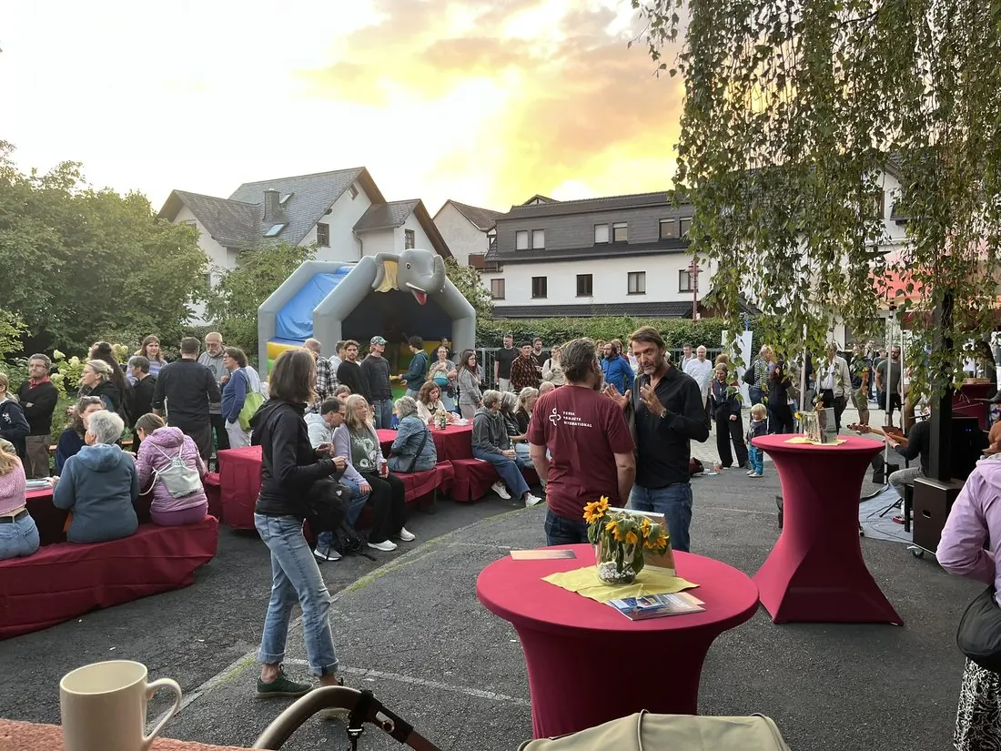 Der Geschäftsführer von TERRA Projekte International im Gespräch auf dem Jubiläumsfest; im Hintergrund sitzen Besucherinnen an Stehtischen.
